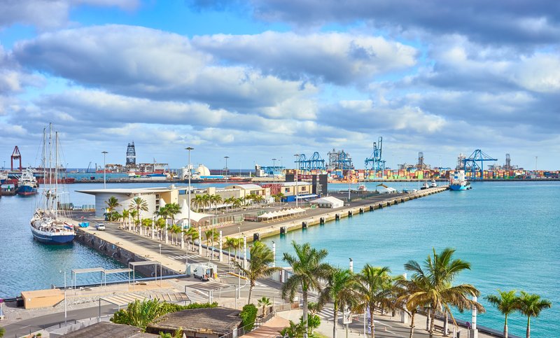 A wide view of the commercial harbor of Las Palmas, featuring cargo ships, cranes, and industrial infrastructure along the coastline.